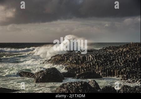 Ocean waves smashing on hexagonal rocks at the giant 's causeway on a murky day. Sea wave hitting a cliff convey a strong impact or big effect concept Stock Photo