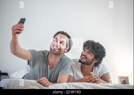 Two gay men taking selfies in the bedroom Stock Photo