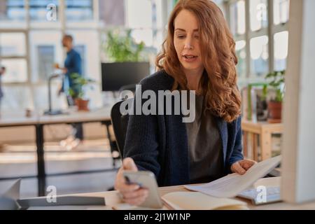 Businesswoman checking her phone while working at her office desk Stock Photo