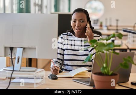 African businesswoman taking notes while talking with a client on her phone Stock Photo