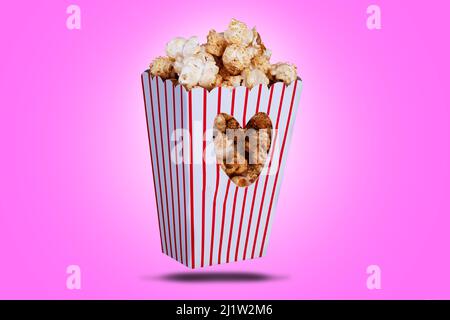 Popcorn in a box with a love heart cutout. Red striped packaging with snack food and a pink background Stock Photo