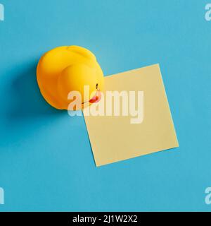 Empty yellow sticky note paper with a rubber duck toy on blue background. Stock Photo