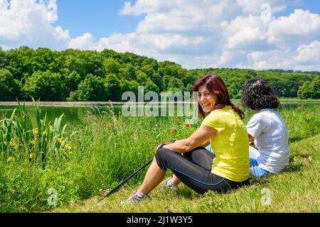 Two sporty women doing pause during a Nordic walking exercise by a small pond Stock Photo