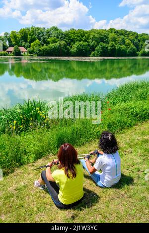 Two sporty women doing pause during a Nordic walking exercise by a small pond Stock Photo