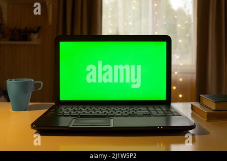 Laptop Computer with Green Mock-up Screen. Green Screen Device Stands on a Desk in the Living Room. Background Cozy Home with Christmas Decoration Stock Photo