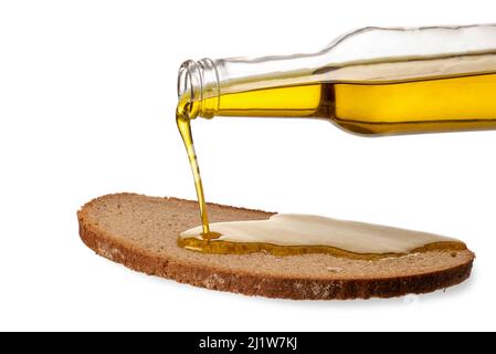 Extra virgin olive oil pouring from glass bottle onto slice of rye bread, isolated on white, clipping path Stock Photo