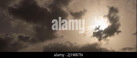 Dark clouds drift across the sky as sunlight glows through a bright opening. The moody cloudscape creates a dramatic and atmospheric weather backgroun Stock Photo