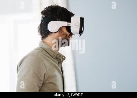 Concentrate young ethnic guy with dark hair and beard in casual clothes with modern VR goggles while exploring cyberspace in daylight Stock Photo