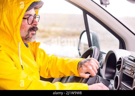 Bearded male driver with hands on steering wheel driving car in countryside Stock Photo