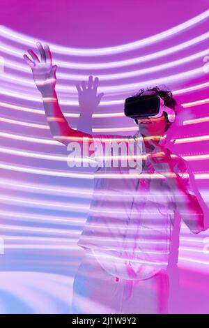 Male in modern VR goggles standing on white background in studio with glowing lights Stock Photo