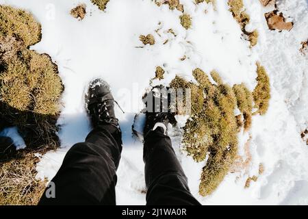 Top view legs of crop anonymous hiker standing on mountain slope covered with snow during trekking in nature on winter day Stock Photo