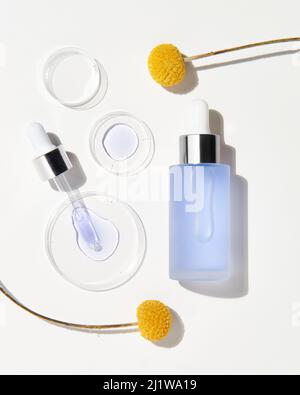 Top view of bottle and pipette with hyaluronic acid for skin care treatment placed on white background with yellow flowers Stock Photo