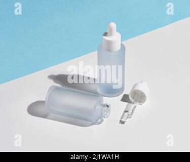 Empty glass bottle with pipettes of natural Hyaluronic acid for skin care treatment placed on two color background under bright sunlight Stock Photo