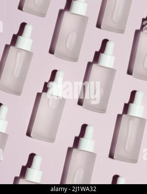 From above background with seamless pattern of many bottles filled with hyaluronic acid placed on pink background in light room Stock Photo