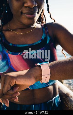 Crop African American female wearing sportswear checking health indicators on tracker after outdoor workout in sunny day Stock Photo