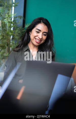 Smiling female entrepreneur browsing netbook during remote work on project in coffee shop Stock Photo