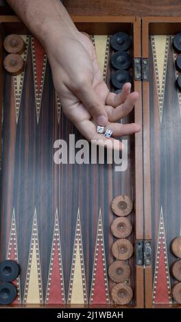 Close up woman hand holding backgammon dices and playing backgammon at outside. The focus is on her hand. Stock Photo