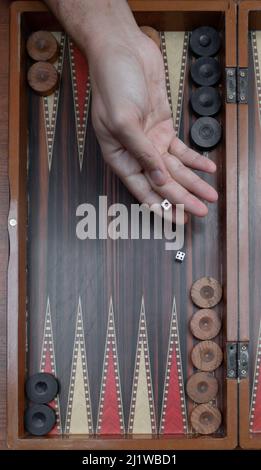 Close up woman hand holding backgammon dices and playing backgammon at outside. The focus is on her hand. Stock Photo