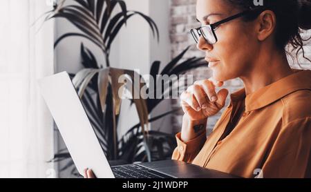 Side view of female people reading and using laptop computer concentrated. Smart working at home. Adult woman with eyewear working online. Modern life Stock Photo