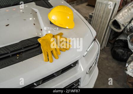 Construction Safety Yellow Plastic Hard Hat and Working Gloves on White Pickup Hood Close Up. Industrial Theme. Stock Photo