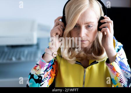 Close-up portrait of focused middle-aged woman wearing headphones watching webinar at office computer Stock Photo