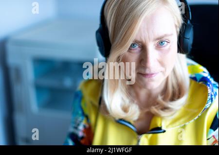 Smiling middle-aged business woman with headphones looking at camera while sitting at office Stock Photo