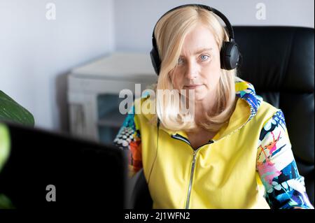 Serious middle-aged business woman with headphones looking at camera while sitting at office Stock Photo
