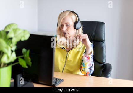 Close-up portrait of focused middle-aged woman wearing headphones watching webinar at office computer Stock Photo