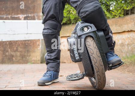 Close up of the legs & feet of an electric unicycle rider resting isolated outdoors on canal towpath, foot resting on footrest. Stock Photo