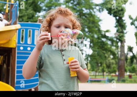 curly kid blowing soap bubbles on playground Stock Photo