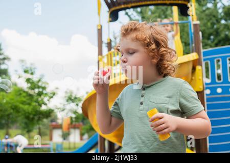 curly boy blowing soap bubbles on playground Stock Photo