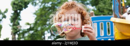 boy blowing soap bubbles outdoors in park, banner Stock Photo