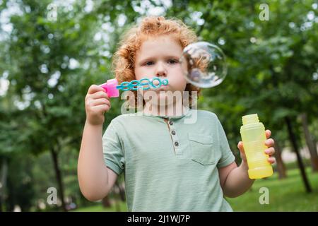 redhead boy blowing soap bubble in summer park Stock Photo