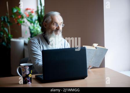 senior man reading book and using laptop computer Stock Photo
