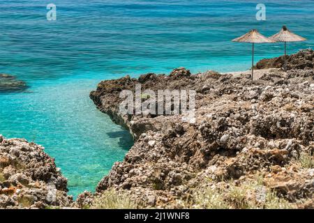 Beautiful empty wild rocky beach with sun umbrellas and beautiful calm sea water Stock Photo