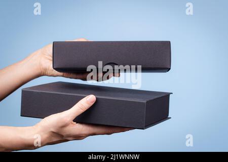 Female hands holding two elegant black cardboard boxes on light blue background. Present, shopping, free shipping, delivery concept Stock Photo