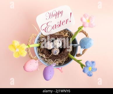Easter card with decorations - nest of quail eggs, decorative color eggs, knitted flowers, note with congratulation Happy Easter in blue bucket on pas Stock Photo