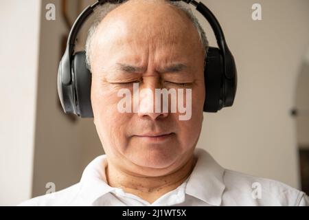 A matured man relaxing at home listening to music with a pair of headphones. Stock Photo