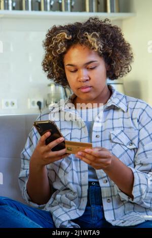 A young African-American woman pays through her smartphone at home Stock Photo