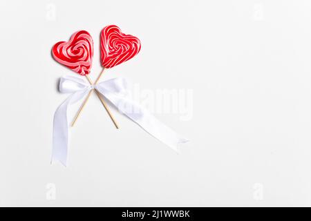 Two heart-shaped lollipops on a stick with a white bow on a white background. Stock Photo