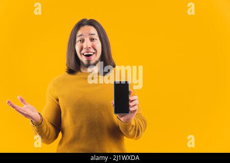 Caucasian bearded man surprised and amazed by huge sales holding mock-up black screen smartphone. Studio shot over yellow background. High quality photo Stock Photo