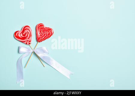Two heart-shaped lollipops on a stick with a white bow on a light blue background. Stock Photo