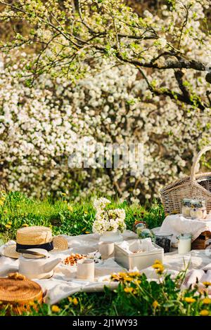 Breakfast picnic with waffles and tea in spring blossom garden on a white tablecloth on a sunny day, cherry blossoms. Outdoor, picnic, brunch, spring Stock Photo