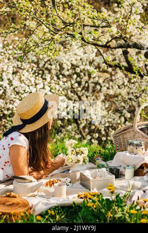 Breakfast picnic with waffles and tea in spring blossom garden on a white tablecloth on a sunny day, cherry blossoms. Outdoor, picnic, brunch, spring Stock Photo