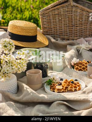 Breakfast picnic with waffles and tea in spring blossom garden on a white tablecloth on a sunny day, cherry blossoms. Outdoor, picnic, brunch, spring Stock Photo