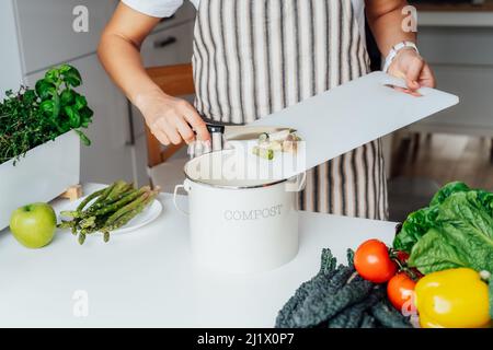 Compost the kitchen waste, recycling. Household woman scraping, throwing vegetables cutting leftovers into the garbage, compost bin while cooking on h Stock Photo