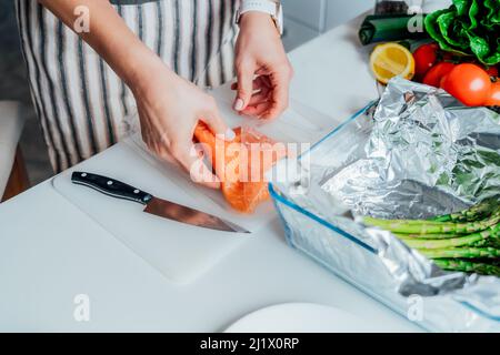 Baked salmon with green asparagus recipe steps. Step one. Woman planning to slice fresh salmon on cutting board. Step by step recipe. Healthy cooking Stock Photo
