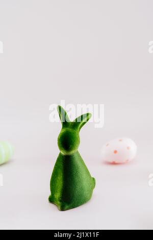 Green bunny rabbit figurine and colored easter eggs in different patterns on neutral pink background. Festive Ester spring vertical card mockup. Selec Stock Photo