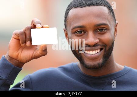 Front view of a happy man with black skin showing blank credit card in the street Stock Photo