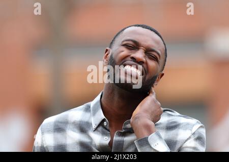 Front view portrait of a man with black skin with neck ache complaining in the street Stock Photo